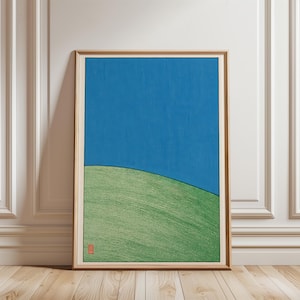 May include: A framed vertical print featuring a solid blue sky above a textured green hill. The artwork is enclosed in a light-colored wooden frame and includes a small red square seal mark in the bottom left corner of the image area.