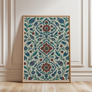 Puede incluir: Impresión artística enmarcada con un diseño floral simétrico en rojo, azul y verde sobre un fondo crema. El marco de madera clara añade calidez. La obra de arte se exhibe contra una pared blanca y un suelo de madera.