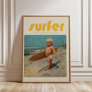 May include: Framed vintage-style poster featuring a young child on a beach holding a surfboard. The poster has the word "surfer" in yellow block letters at the top, with "The Saltwater Society" below. The bottom of the poster reads "Ride the Tide, Join the Tribe."