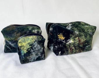 Puede incluir: Tres neceseres de terciopelo de diferentes tamaños. Las bolsas presentan un estampado abstracto en verde oscuro, negro y dorado con cremalleras plateadas. La bolsa más grande tiene un adorno de hoja dorada.