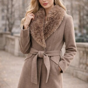 Peut inclure: Un long manteau marron clair avec un col en fausse fourrure et une ceinture assortie nou&eacute;e &agrave; la taille. Le manteau a un design classique avec une coupe ajust&eacute;e et des poches. Le mod&egrave;le porte le manteau &agrave; l'ext&eacute;rieur.