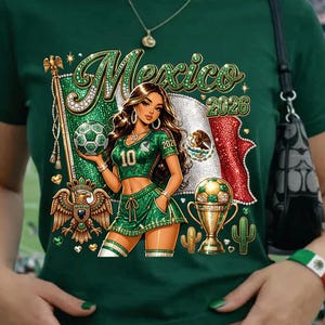 May include: A dark green t-shirt featuring a graphic print of a person in a green soccer uniform, a soccer ball, a gold trophy, a Mexican flag, and the text "Mexico 2026". The design includes a golden eagle emblem and small cactus icons.