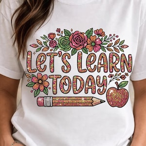 May include: A white short-sleeved t-shirt featuring a colorful graphic with the text "LET'S LEARN TODAY" in a dotted pattern. The design includes pink and green flowers, a yellow pencil, and a red apple, all rendered with a textured, glittery appearance.