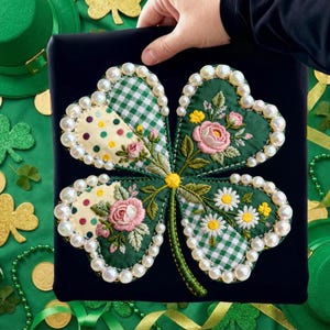Può includere: Un quadrato nero con un design a quadrifoglio. Il quadrifoglio è verde con fiori ricamati e motivi a quadretti. I bordi sono bordati con perle finte. Lo sfondo include cappelli verdi, trifogli e monete d'oro.