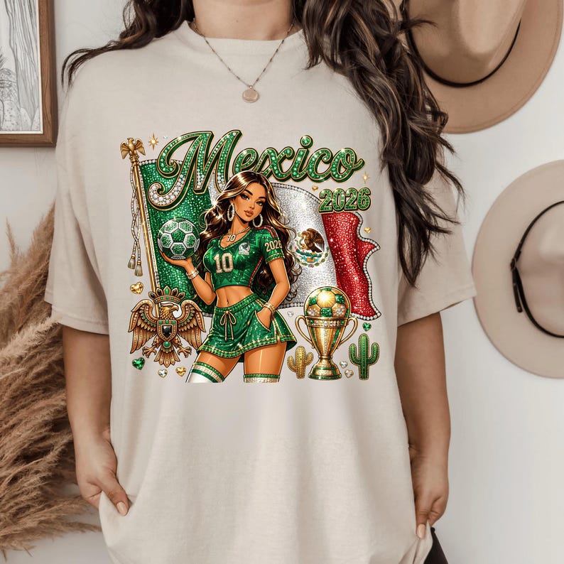 May include: A beige t-shirt featuring a graphic of a person in a green soccer uniform holding a soccer ball. The design includes the text Mexico 2026, a Mexican flag, a golden eagle emblem, a trophy, and cacti, all rendered in a glittery style.
