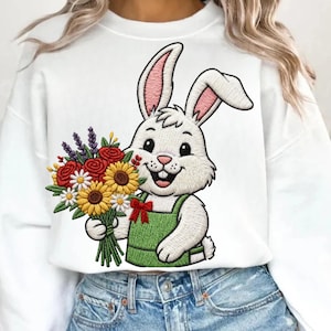 May include: White sweatshirt featuring an embroidered cartoon bunny holding a bouquet of flowers. The bunny wears green overalls and a red bow. The bouquet includes sunflowers, daisies, and roses.