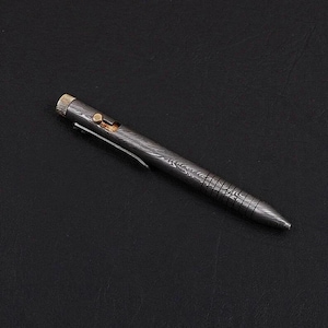 Puede incluir: Un bolígrafo gris oscuro con un patrón texturizado y detalles dorados. El bolígrafo tiene un clip y un mecanismo de botón. El cuerpo del bolígrafo tiene un patrón único y arremolinado, y la punta es puntiaguda.