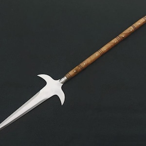 May include: A spear with a polished steel blade and a wooden shaft. The blade has a unique shape with two curved protrusions. The shaft is light brown with decorative silver accents and small white dots. The spear is set against a dark background.
