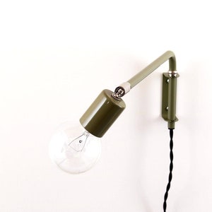 May include: A green metal wall-mounted lamp with a black cord and a clear light bulb. The lamp has a simple design and is adjustable.
