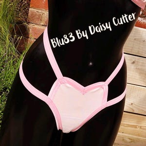 Puede incluir: Lingerie rosa en forma de corazón con un diseño de tirantes rosas. La lencería está etiquetada como "Blu83 By Daisy Cutter".