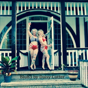 Puede incluir: Dos mujeres en lencería roja y negra posan frente a una casa blanca y negra con un porche. El texto "Blu83 by Daisy Cutter" está en la parte inferior de la imagen.
