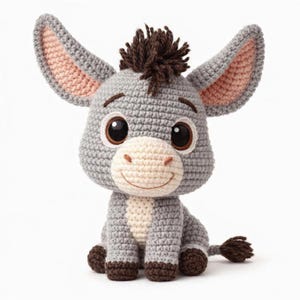 May include: A crocheted donkey toy in shades of gray, brown, and cream. The donkey has large, expressive eyes, long ears with pink inner linings, and a tuft of brown hair. It is sitting upright with a smiling face and a small tail.