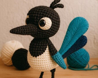 May include: A crocheted magpie bird, featuring black, white, and teal blue yarn. The bird has large eyes and a long beak. It stands on a wooden surface, with balls of yarn visible in the background.