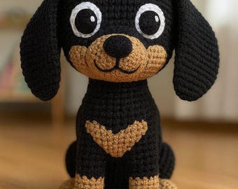 Puede incluir: Un perro de ganchillo hecho a mano en negro y marrón claro. El perro amigurumi tiene ojos grandes y redondos, orejas caídas y una cara sonriente. El perro está sentado sobre sus cuartos traseros, mostrando sus patas y un patrón de chevrón en su pecho.