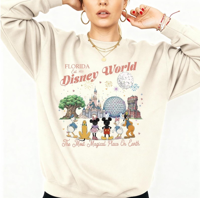 May include: A cream-colored crewneck sweatshirt featuring a graphic print of Disney World landmarks and characters. The text reads Florida Est 1971 Disney World The Most Magical Place On Earth. The design includes Mickey, Minnie, Donald, Daisy, and Pluto.