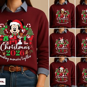 May include: A maroon crewneck sweatshirt featuring a graphic of a Disney character wearing a Santa hat, surrounded by Christmas trees, candy canes, and the text Family Christmas 2026 making memories together in red, green, and white colors.