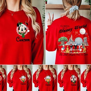 May include: A red crewneck sweatshirt featuring a small graphic of Mickey Mouse in a holiday hat on the left chest with the word Custom below it. The back displays a large Disney World Florida graphic with characters and park landmarks.