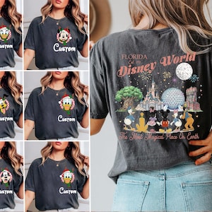 May include: A charcoal grey t-shirt featuring a small circular Disney character graphic on the front left chest with the word Custom below it. The back displays a large colourful illustration of Disney World landmarks and characters with the text Florida Disney World The Most Magical Place On Earth.