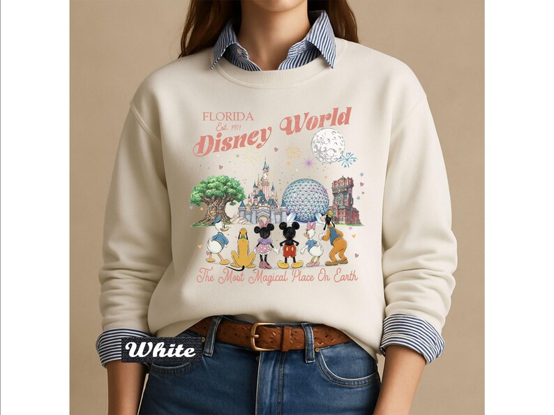 May include: A cream-colored crewneck sweatshirt featuring a graphic print of Disney characters and landmarks. The text reads Florida Est. 1971 Disney World and The Most Magical Place On Earth. The design includes Mickey, Minnie, Donald, Daisy, Pluto, and Goofy.