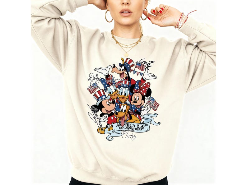 May include: A cream-colored crewneck sweatshirt featuring a graphic print of Disney characters including Mickey Mouse, Minnie Mouse, Donald Duck, Daisy Duck, Goofy, and Pluto wearing patriotic hats, with the text America 250th USA Anniversary.