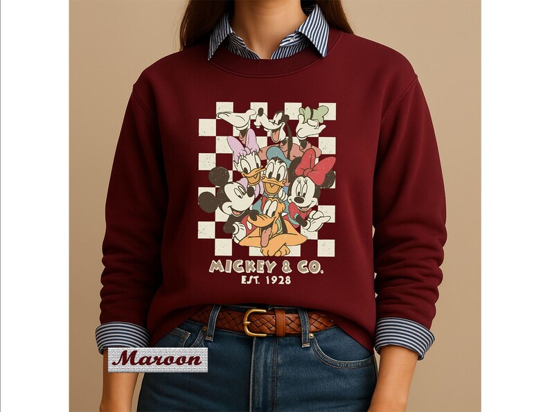 May include: A maroon crewneck sweatshirt featuring a graphic print of Mickey Mouse, Minnie Mouse, Donald Duck, Daisy Duck, Goofy, and Pluto over a white and maroon checkerboard pattern. The text MICKEY & CO. EST. 1928 is printed below the characters.
