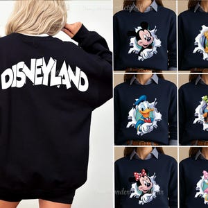 May include: A black long-sleeve sweatshirt featuring the word Disneyland in large white letters on the back. The front displays various Disney character graphics, including Mickey Mouse, Pluto, Donald Duck, Goofy, Minnie Mouse, and Daisy Duck.
