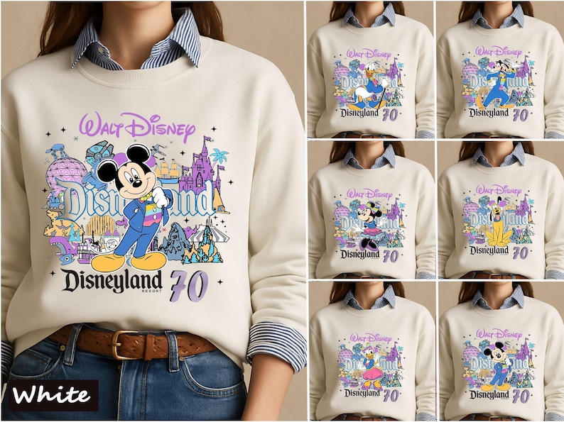 Op de afbeelding: Een cr&egrave;mekleurig sweatshirt met ronde hals en een grafische print van Walt Disney Disneyland 70 met diverse Disney-figuren zoals Mickey Mouse, Donald Duck en Goofy, gedragen over een blauw-wit gestreept overhemd.