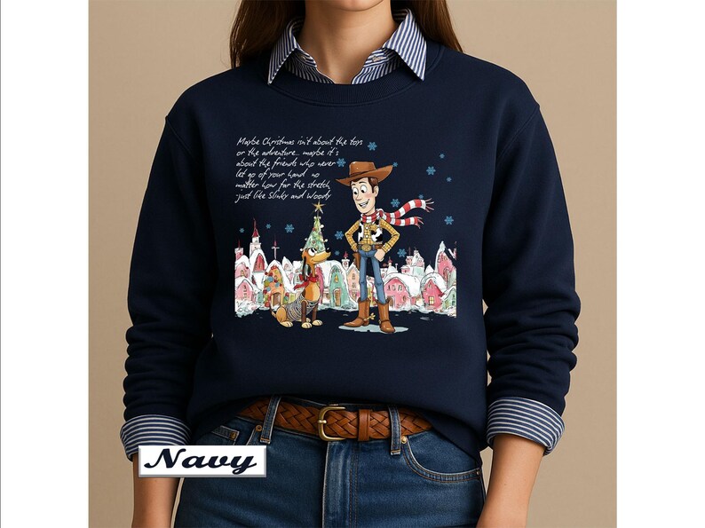 May include: A navy blue long-sleeve sweatshirt featuring a graphic of Woody and Slinky Dog from Toy Story in a snowy village setting. The text reads: Maybe Christmas isn't about the toys or the adventure, maybe it's about the friends who never let go of your hand no matter how far the stretch, just like Slinky and Woody.
