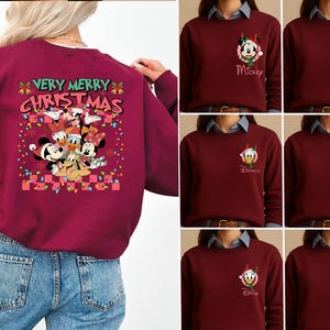 May include: A maroon sweatshirt featuring a large back graphic with the text VERY MERRY CHRISTMAS and Disney characters including Mickey, Minnie, Donald, Daisy, Goofy, and Pluto. The front chest area displays a small character icon with a name.