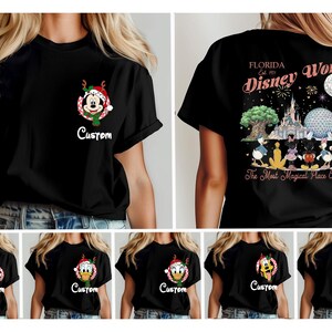 May include: A black t-shirt featuring a small graphic on the front left chest of a character in a Christmas wreath with the word Custom below it. The back displays a large Disney World graphic with characters, landmarks, and the text The Most Magical Place On Earth.