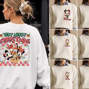 May include: A white crewneck sweatshirt featuring a large back graphic with the text "VERY MERRY CHRISTMAS" and a colorful illustration of Disney characters in holiday attire. The front chest area displays smaller individual character prints.