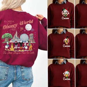 May include: A maroon long-sleeve sweatshirt featuring a large back graphic of Disney World landmarks and characters with the text Florida Est. 1971 Disney World The Most Magical Place On Earth. The front chest displays a small character and Custom text.