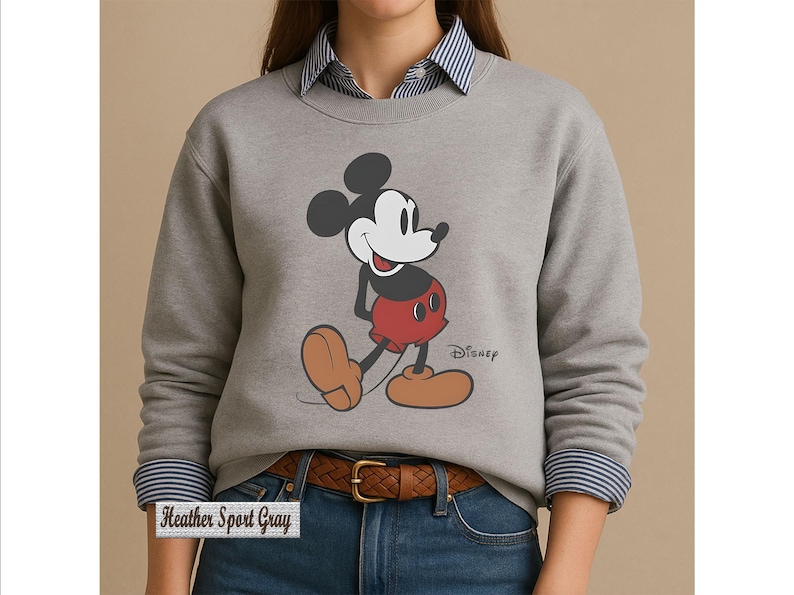 May include: A heather sport gray crewneck sweatshirt featuring a graphic of Mickey Mouse in his classic red shorts and tan shoes. The Disney logo is printed in black next to the character. The sweatshirt is worn over a blue and white striped shirt.