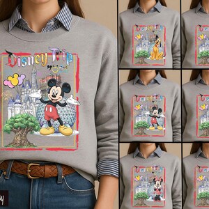 May include: A sport gray crewneck sweatshirt featuring a graphic print with the text Disney Trip, a castle, a large tree, and Mickey Mouse. The design includes colorful balloons and a geodesic sphere. Additional variations show Pluto, Goofy, Daisy, Minnie, and Donald.