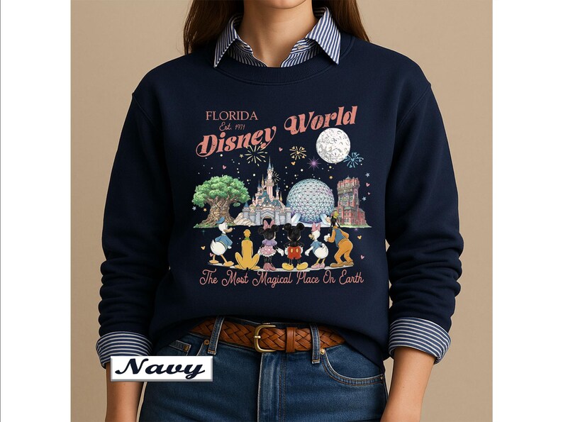 May include: A navy blue long-sleeve sweatshirt featuring a graphic print of Disney World landmarks and characters. The text reads Florida Est. 1971 Disney World and The Most Magical Place On Earth. The design includes a moon, fireworks, and icons.