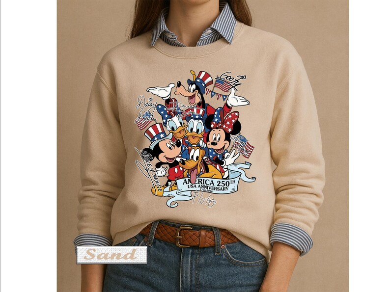May include: A sand-colored crewneck sweatshirt featuring a graphic print of Disney characters including Mickey Mouse, Minnie Mouse, Donald Duck, Goofy, and Pluto wearing patriotic hats. The text reads America 250th USA Anniversary 1776-2026.