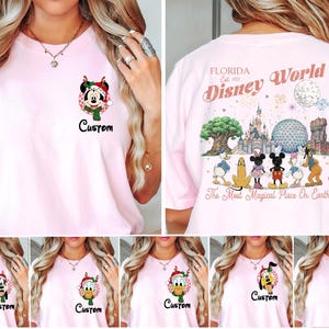 May include: A light pink t-shirt featuring a small graphic on the front left chest of a Disney character in a Christmas hat with the word Custom. The back displays Florida Est. 1971 Disney World with park icons and characters.