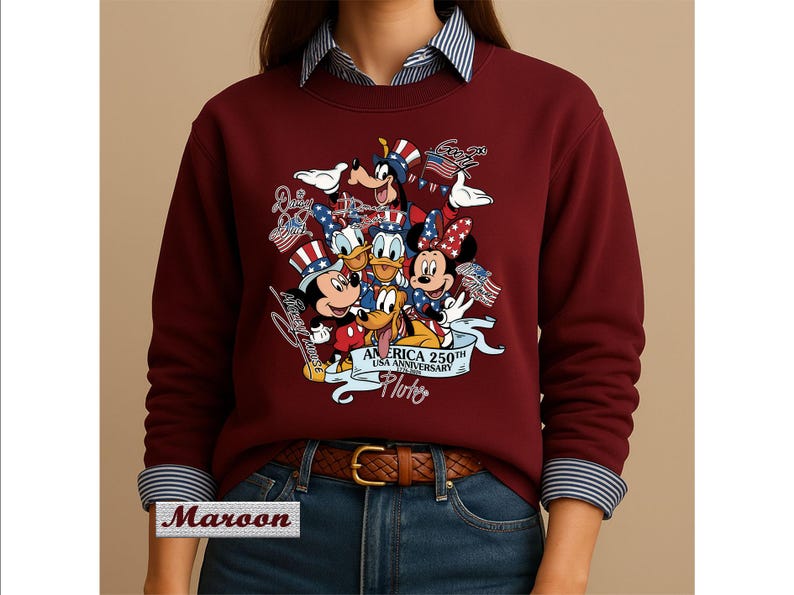 May include: A maroon long-sleeve sweatshirt featuring a graphic print of Disney characters including Mickey Mouse, Minnie Mouse, Donald Duck, Daisy Duck, Goofy, and Pluto wearing patriotic hats. The text reads AMERICA 250TH USA ANNIVERSARY 1776-2026.