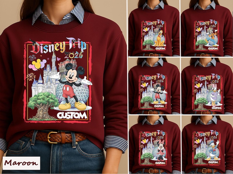 May include: A maroon crewneck sweatshirt featuring a graphic print with the text Disney Trip 2026. The design includes a castle, a large spherical structure, a tree, fireworks, and various Disney characters like Mickey Mouse, Pluto, and Donald Duck.