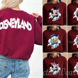 May include: A maroon long-sleeve sweatshirt featuring the word DISNEYLAND in large white letters on the back. The front displays various Disney character graphics, including Mickey Mouse, Pluto, Donald Duck, Goofy, Minnie Mouse, and Daisy Duck.