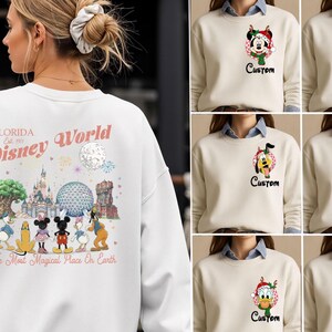 May include: A white crewneck sweatshirt featuring a large back graphic of Disney World landmarks and characters with the text Florida Est. 1971 Disney World The Most Magical Place on Earth. The front features a small circular character print and Custom text.
