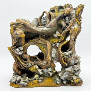Könnte beinhalten: Ein dekoratives Aquarium-Ornament mit einer strukturierten, knorrigen Baumwurzelstruktur mit ineinander verschlungenen Ästen, Felsformationen und hohlen Öffnungen. Das Stück ist in Braun-, Grau- und Gelbtönen gehalten und imitiert Holz und Stein.