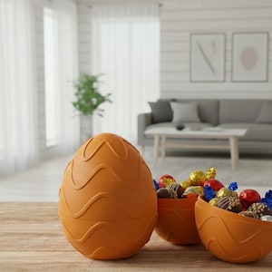 May include: An orange, egg-shaped container with a wavy design, next to two orange bowls filled with wrapped chocolates. The scene is set on a wooden table, with a living room in the background.