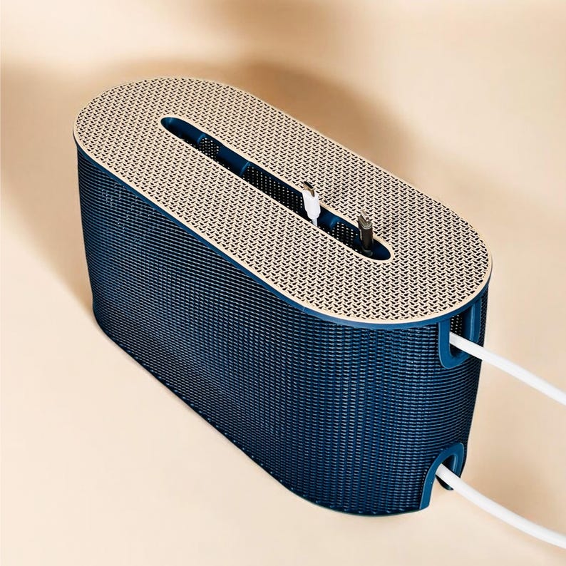 K&ouml;nnte beinhalten: Ein marineblauer Kabelorganizer mit ovaler Form und strukturierter Oberfl&auml;che. Die Oberseite ist beige mit einem gemusterten Design. Wei&szlig;e Kabel ragen aus den Seiten, und Ladekabel sind im Inneren sichtbar.
