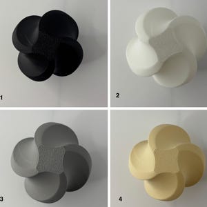 K&ouml;nnte beinhalten: Vier dekorative, bl&uuml;tenf&ouml;rmige Objekte in Schwarz, Wei&szlig;, Grau und Beige. Jedes hat eine strukturierte Mitte und abgerundete Bl&uuml;tenbl&auml;tter. Die Objekte werden vor einem wei&szlig;en Hintergrund pr&auml;sentiert, um ihre Design- und Farbvariationen hervorzuheben.