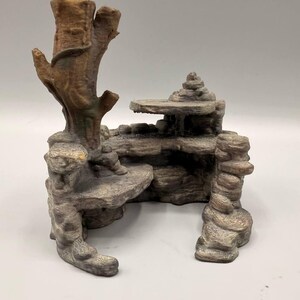 Può includere: Un ornamento per acquario testurizzato marrone e grigio caratterizzato da una struttura a tronco d'albero alta integrata con formazioni rocciose a strati, creando molteplici piattaforme piatte e una piccola apertura a grotta.