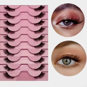 Könnte beinhalten: Ein Set falscher Wimpern, präsentiert auf einem rosa Halter, zusammen mit zwei Nahaufnahmen von Augen mit angebrachten Wimpern. Die schwarzen Wimpern sind voluminös und sollen die Augen optisch betonen.