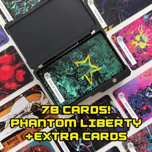 Pode incluir: Um baralho de 78 cartas de tarô Phantom Liberty com cartas extras, apresentando ilustrações coloridas. As cartas são exibidas em torno de um estojo preto, com a carta Rei de Pentáculos visível no interior. O texto nas cartas inclui "O Imperador" e "Seis de Copas."