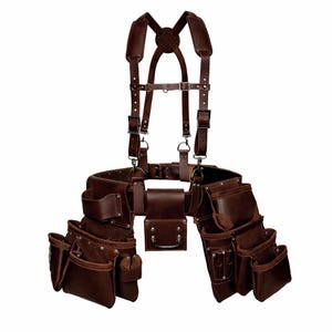 Op de afbeelding: Een bruine leren gereedschapsriem met bretels. De riem heeft meerdere zakken van verschillende maten en een centrale tas met een handvat. De bretels zijn verstelbaar en worden met metalen beslag aan de riem bevestigd.