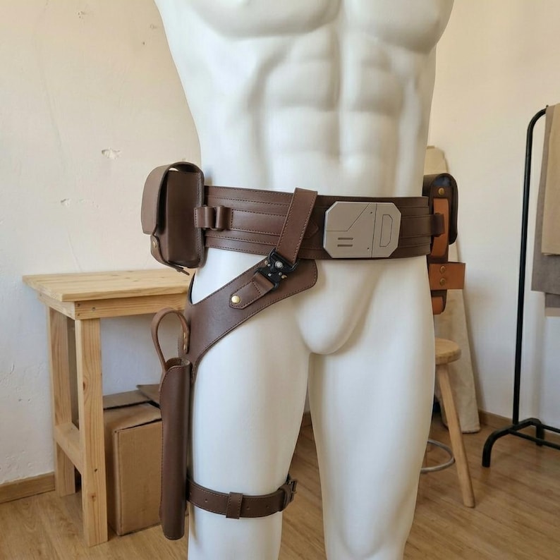 May include: A brown utility belt featuring a rectangular metallic buckle with engraved lines, a side pouch, and a drop-leg holster with a thigh strap. The belt is constructed from leather-like material with metallic hardware and a black tactical buckle.